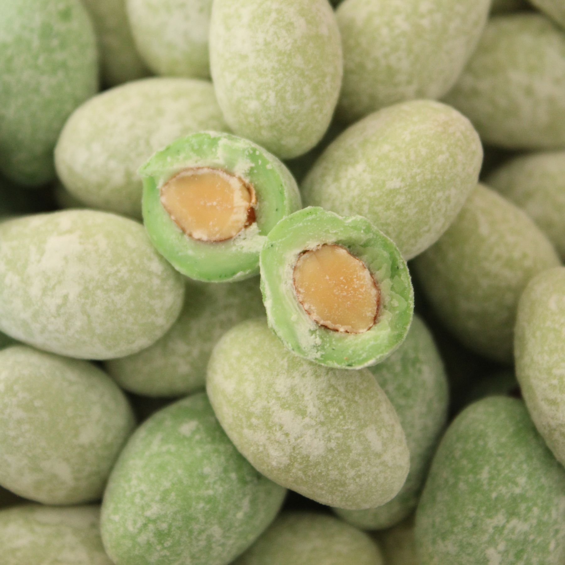 schokolierte Mandelkerne in hellem Gruen auf einem Haufen, eine Mandel aufgeschnitten