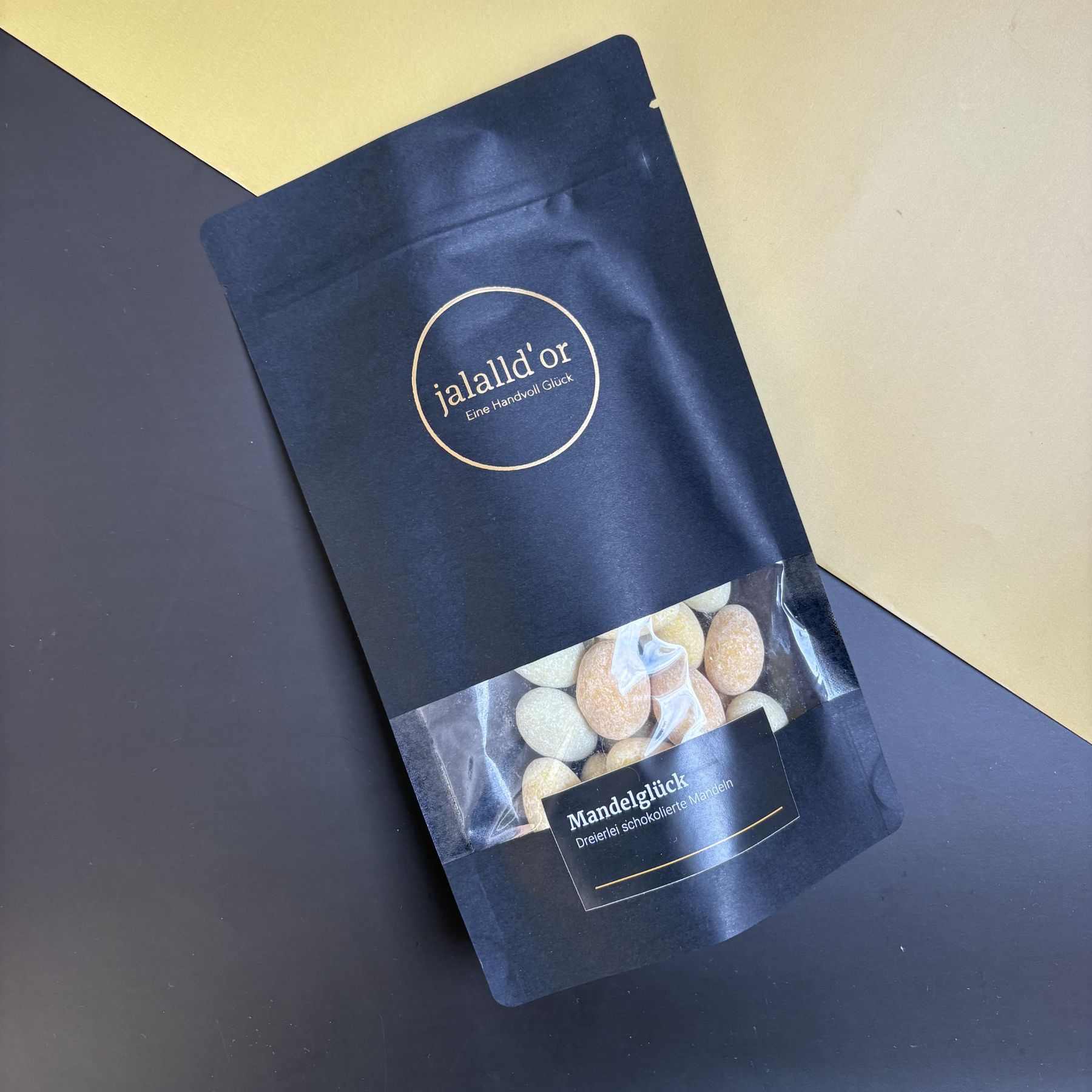 schwarze Geschenkverpackung mit bunten Mandeln liegt auf schwarz gelbem Untergrund
