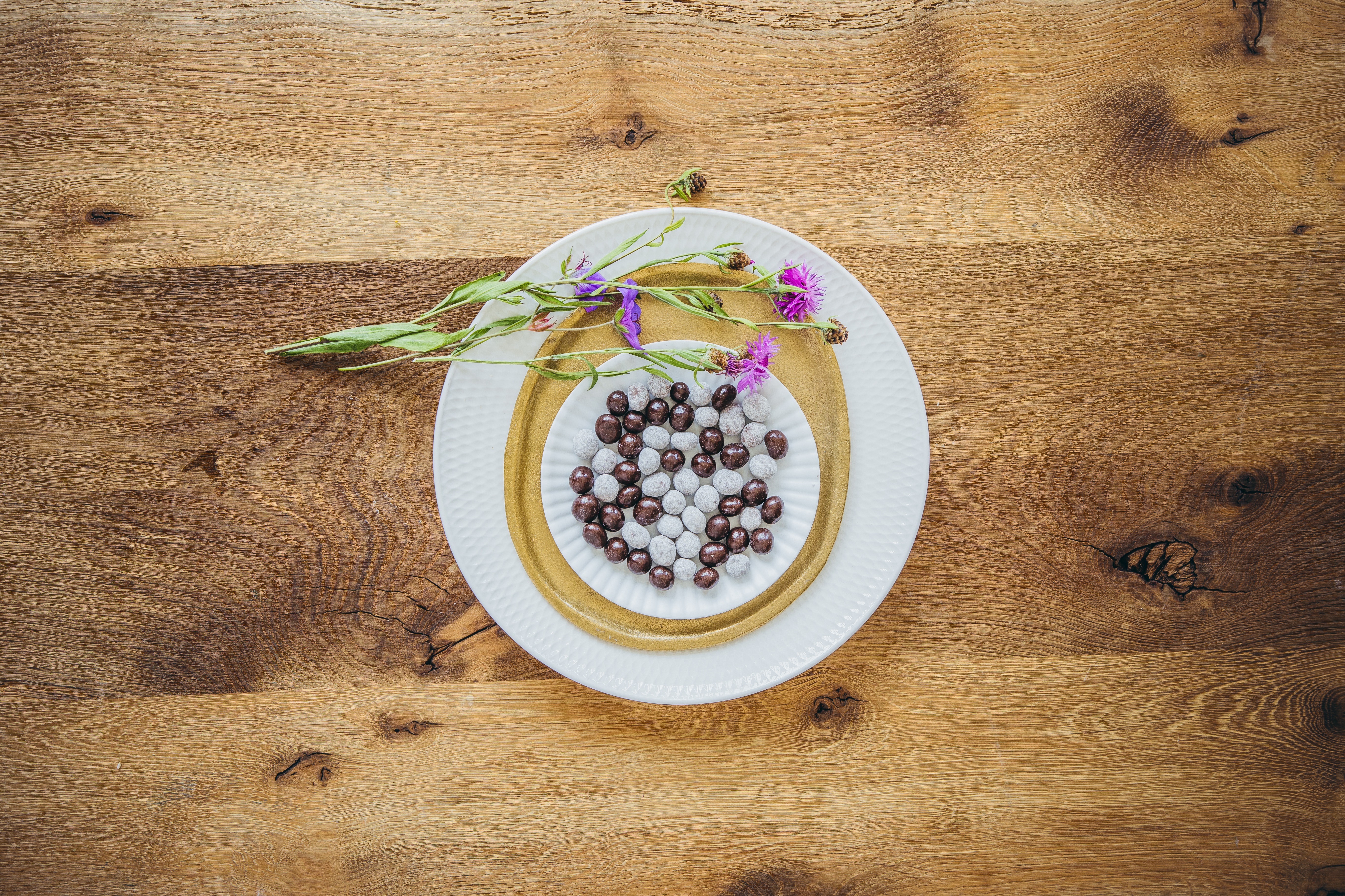 Kaffeebohnen in Schokolade liegen auf Tellern, welche auf einem Holzboden liegen